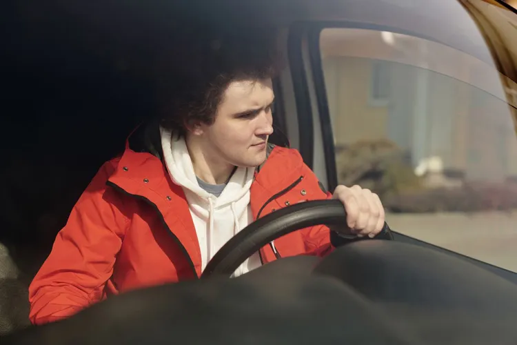 Jonge man geconcentreerd achter het stuur tijdens een rijles in een woonwijk