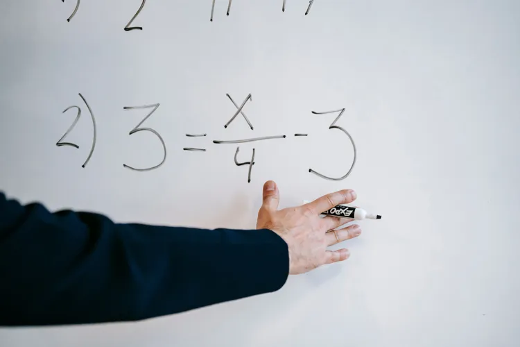 Bijlesdocent legt bij een whiteboard stap voor stap een wiskundevergelijking uit