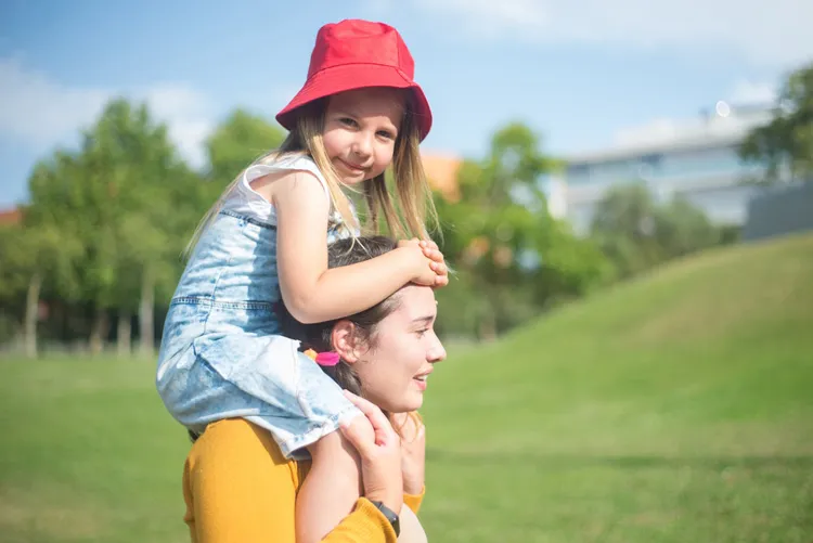 Au pair draagt een lachend kind op haar schouders in het park, vertrouwensband met het gastgezin