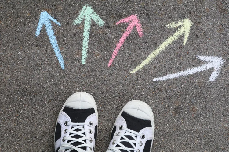 Sneakers van een jongere bij meerdere krijt-pijlen op de stoep — symbool voor het kiezen tussen tussenjaar-mogelijkheden